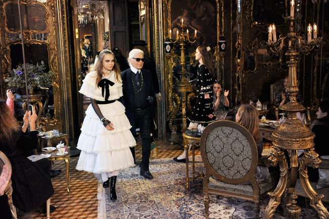 Karl Lagerfeld and Cara Delevingne, wearing a tiered white lace dress, walk through the Schloss Leopoldskron for the finale
